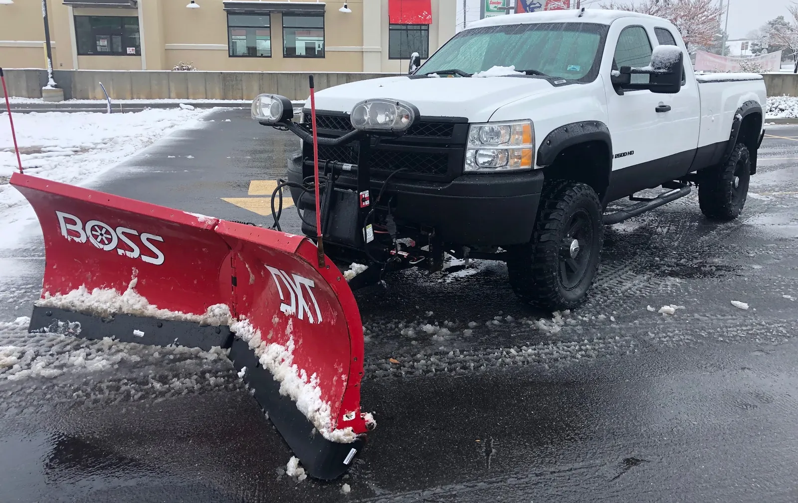 The same All Seasons truck fitted with a red BOSS snow plow, clearing a lot after a storm